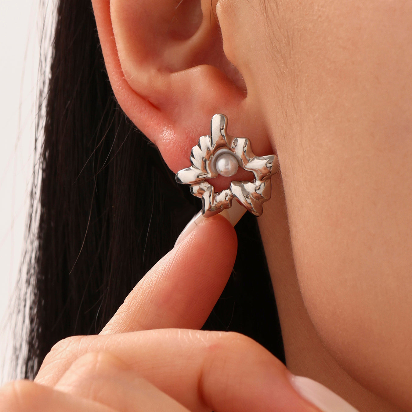 Silver star-shaped earring with a pearl center worn by a person.