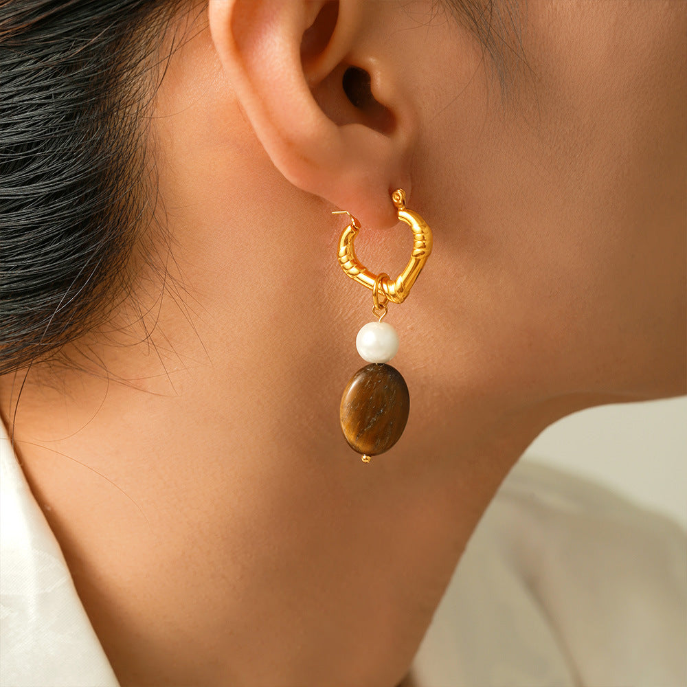 Gold hoop earring with a white pearl and brown stone worn by a person.