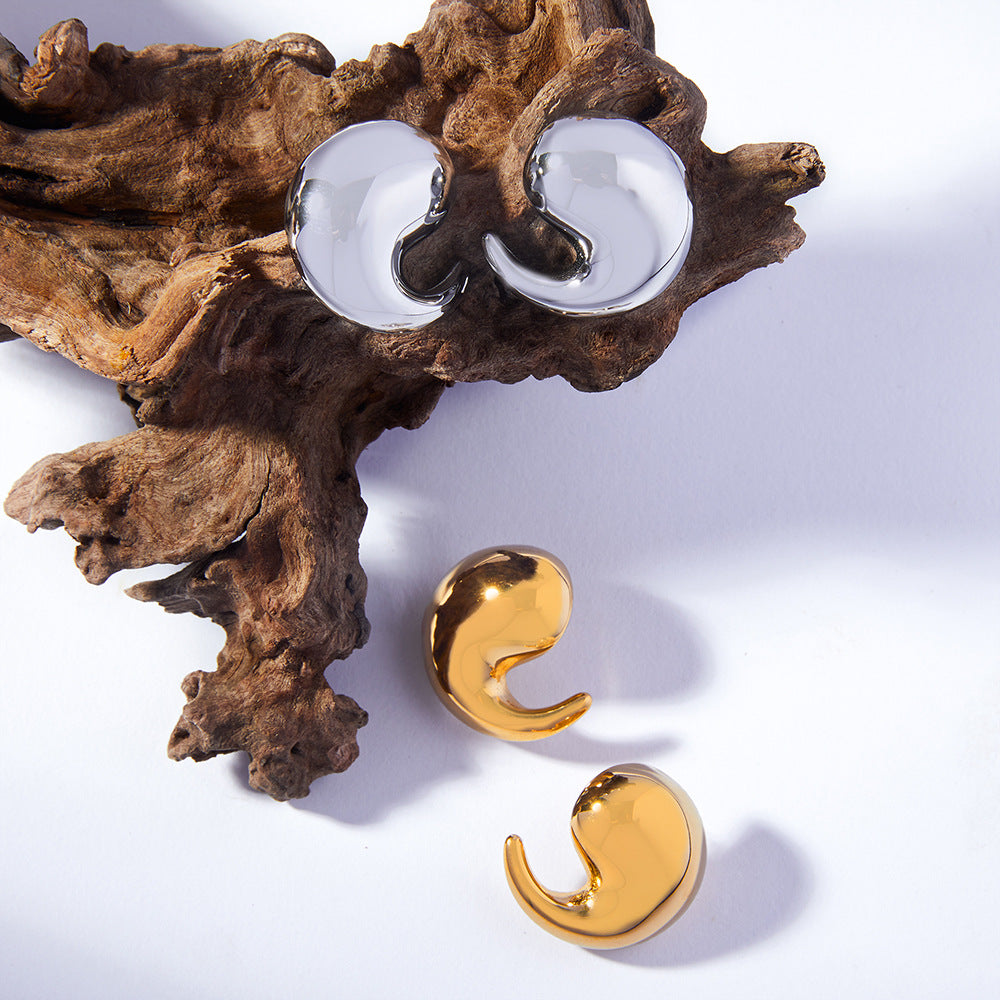 Pair of gold earrings on a white surface with a piece of wood.
