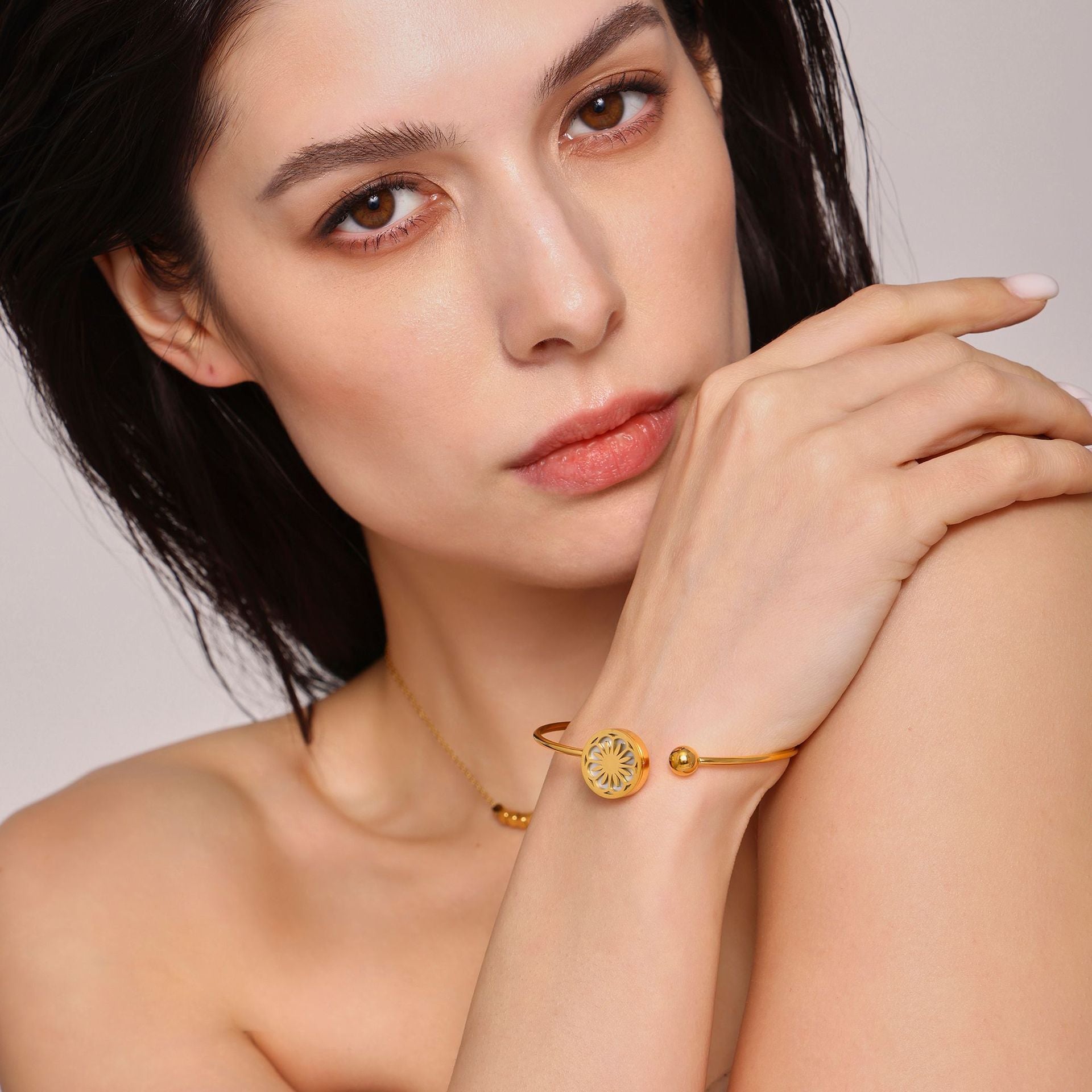 Close-up of woman wearing gold bracelets and necklace on neutral backdrop