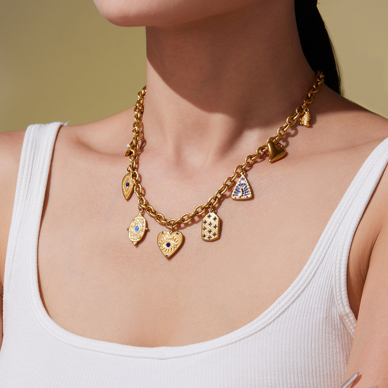 Model wearing the gold blue zircon charm necklace, showing the multi-element geometric pendants and central blue zircon stone resting at the collarbone on a 42+5 cm gold stainless steel chain.