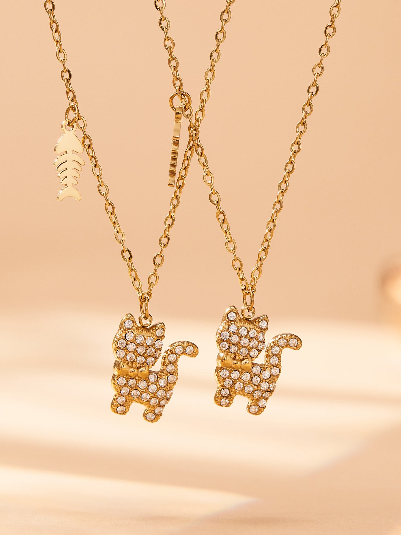 Two gold CZ cat necklaces displayed together to show the pendant detail and fishbone charm movement.