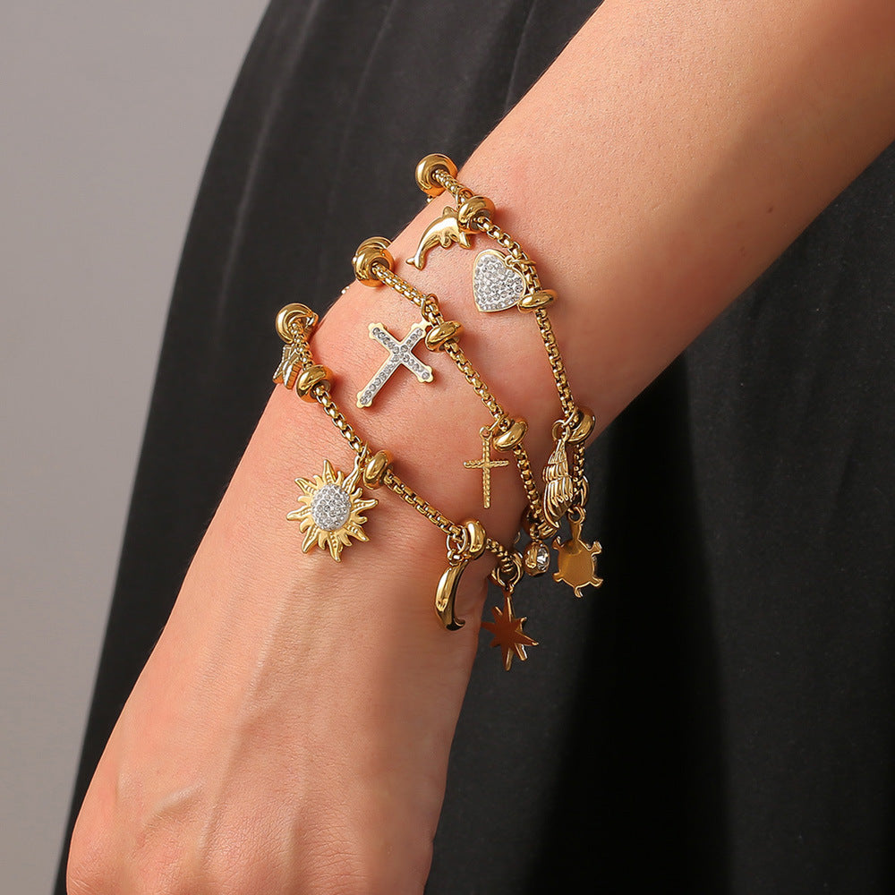 Model wearing gold charm bracelet with multiple pendants on wrist against black background