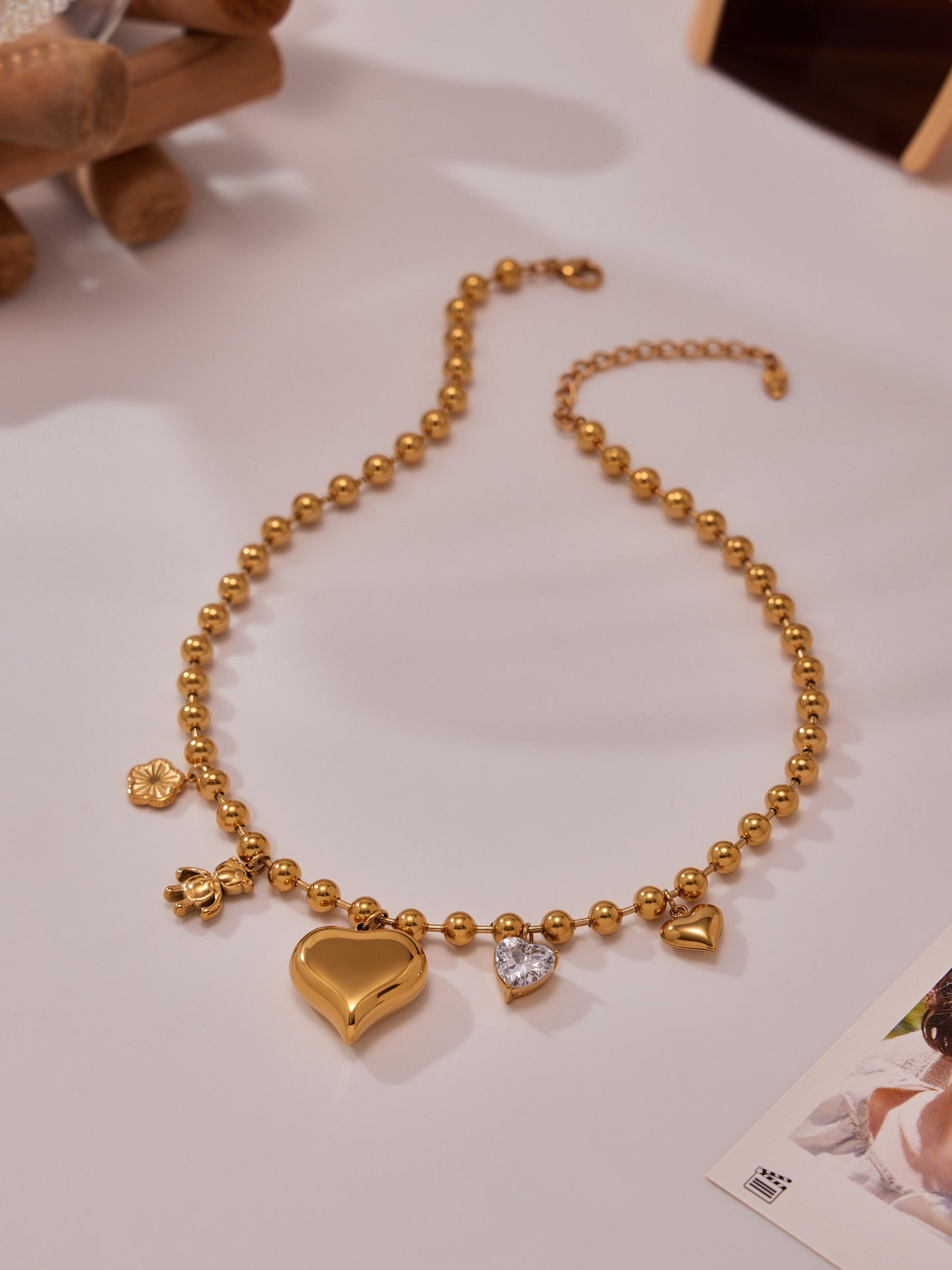Gold heart charm beaded necklace displayed on table, elegant stainless steel love choker jewelry