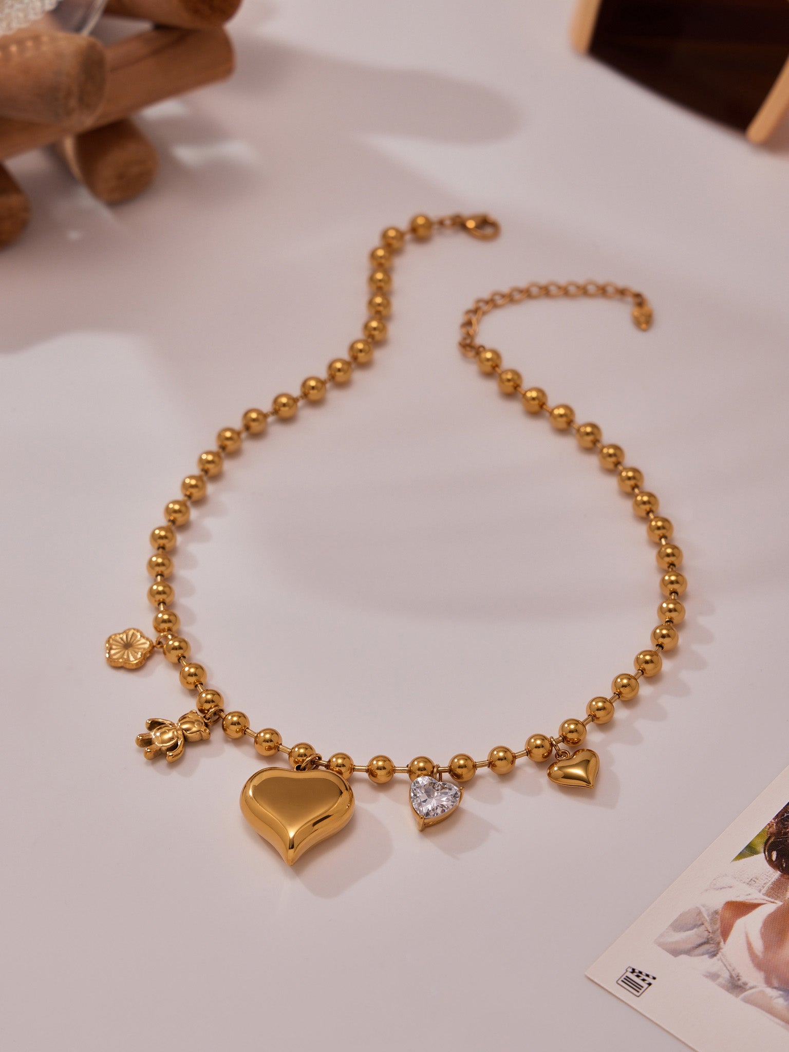 Gold heart charm beaded necklace displayed on table, elegant stainless steel love choker jewelry