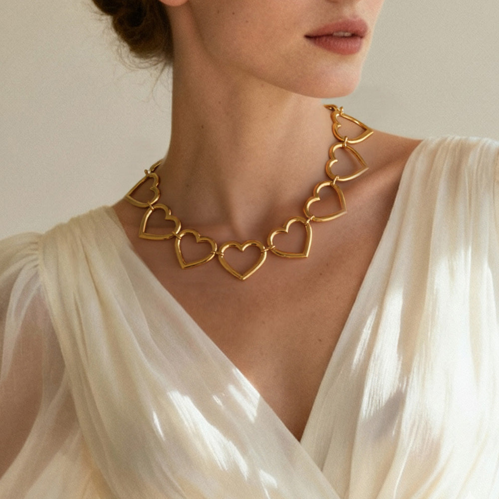 Gold heart-shaped necklace worn by a person in a white garment against a neutral background