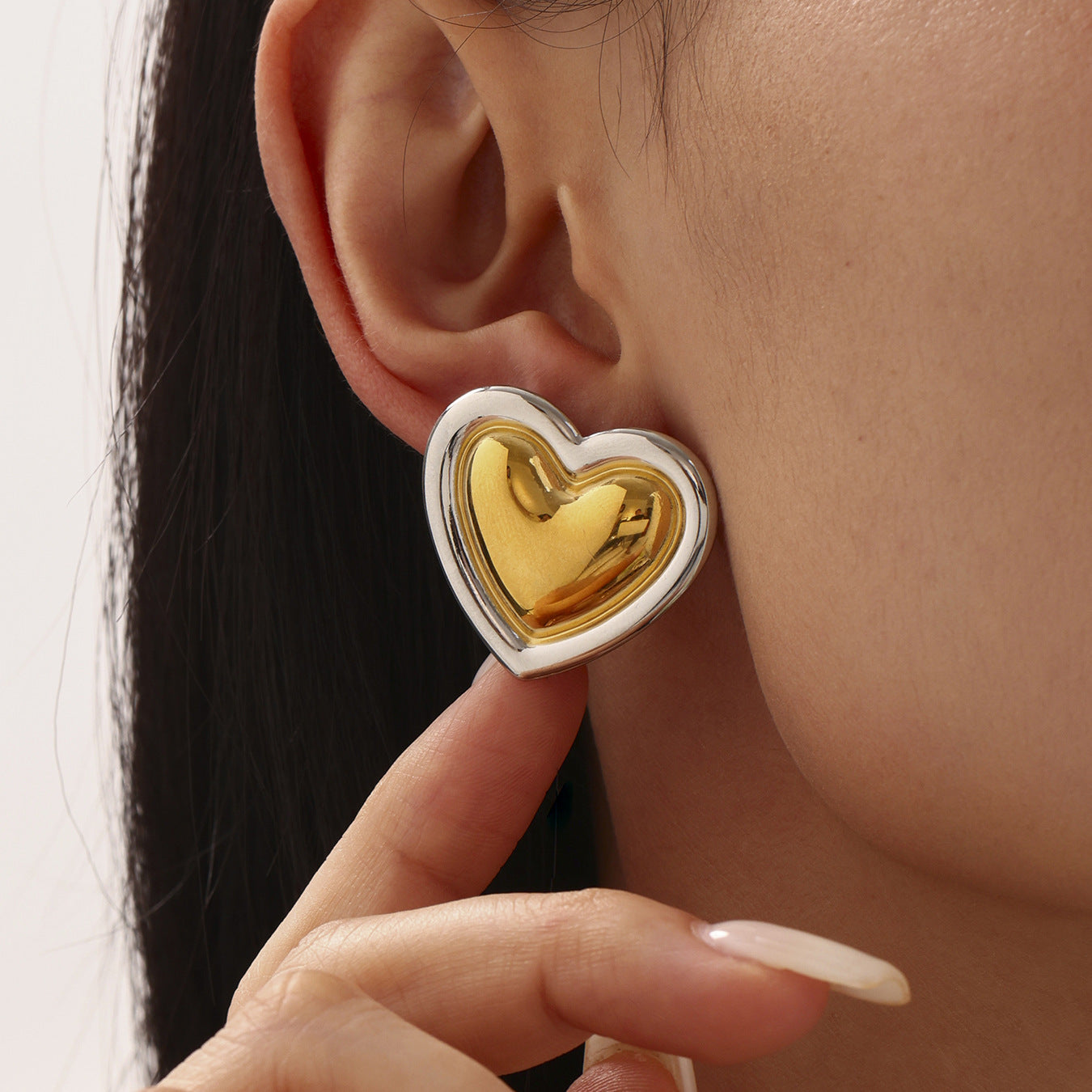 Gold heart-shaped earring worn by a person with a neutral background