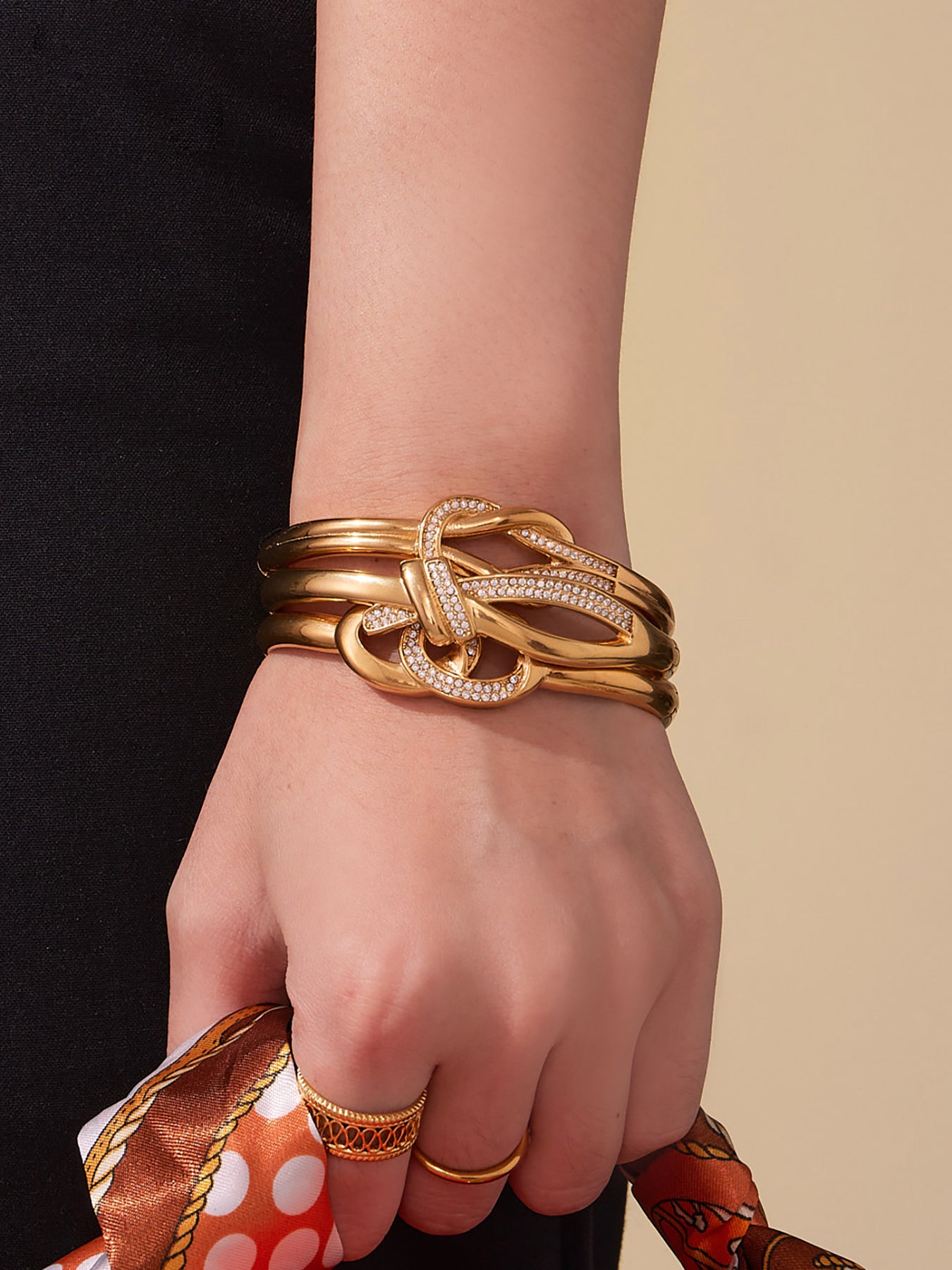 Front view of a model wearing stacked 18K gold knotted cuff bangles, showing the flowing knot shape and glowing waterproof coating in soft natural light.