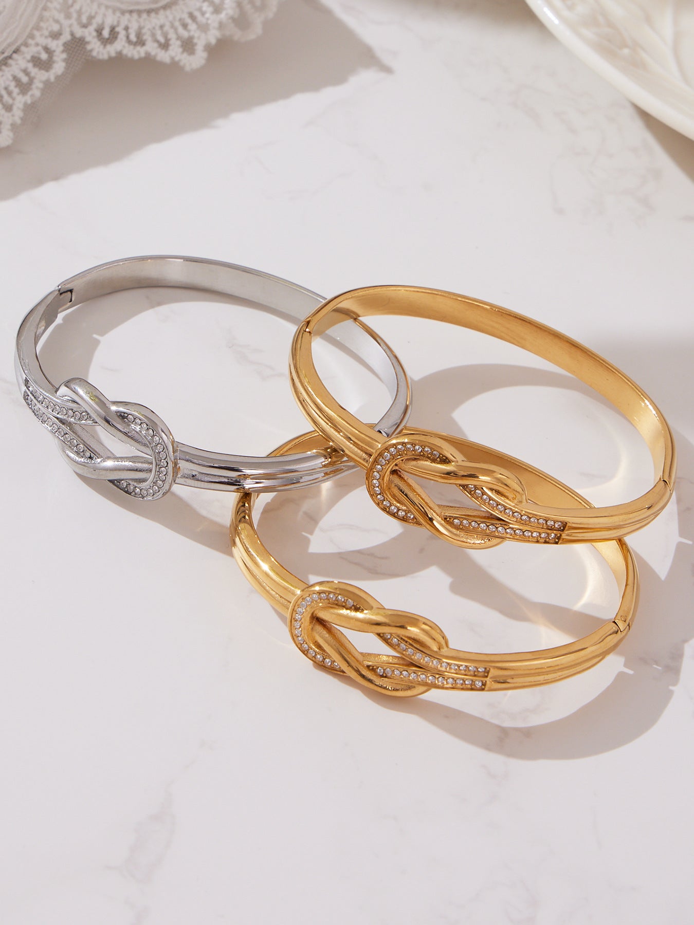Gold and silver knotted cuff bangles arranged together on a marble surface, showing their stacking style, pavé CZ sparkle and Endures-Forever’s signature waterproof polish.