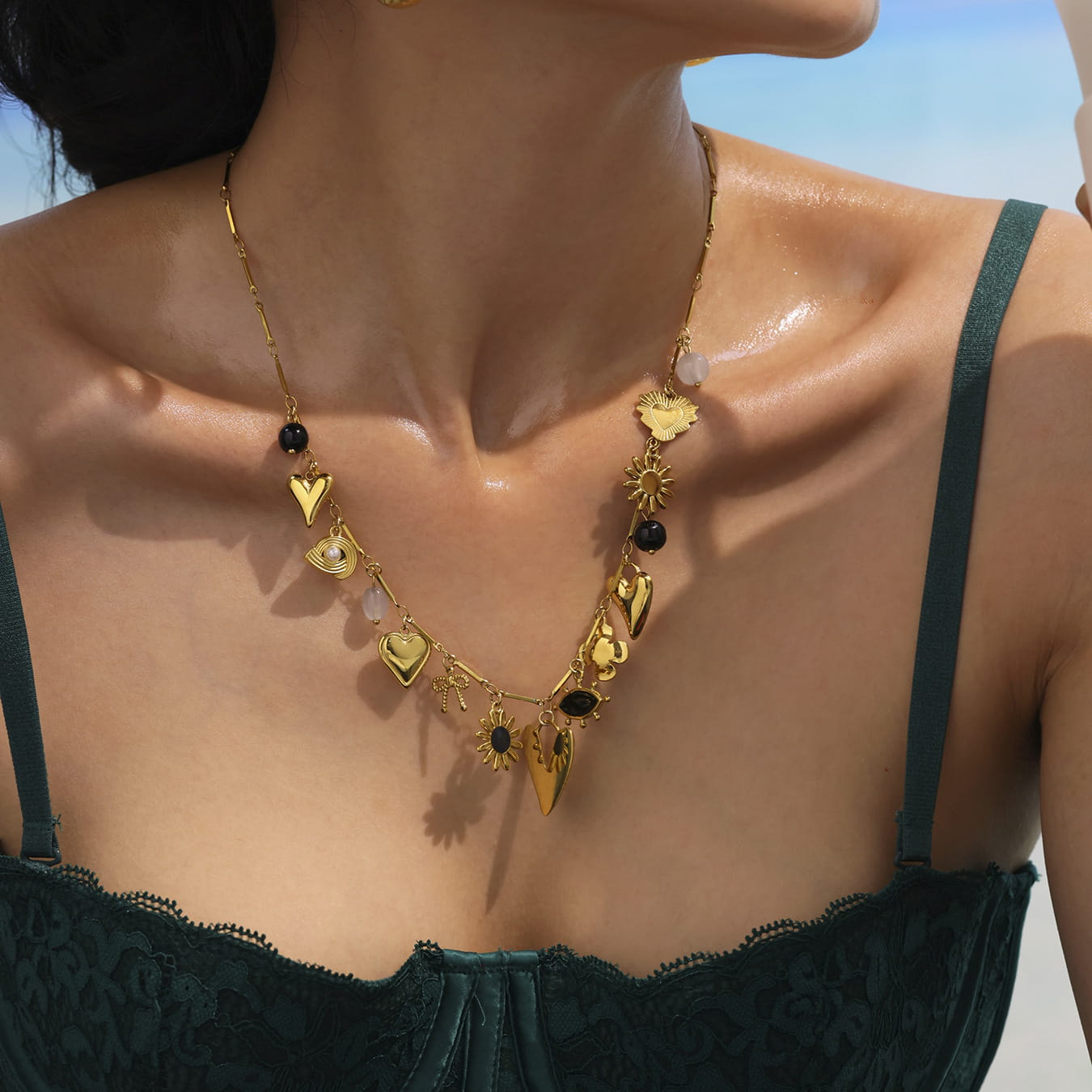 Model wearing gold sun and moon charm necklace with heart pendant, colorful enamel charms and celestial motifs.

