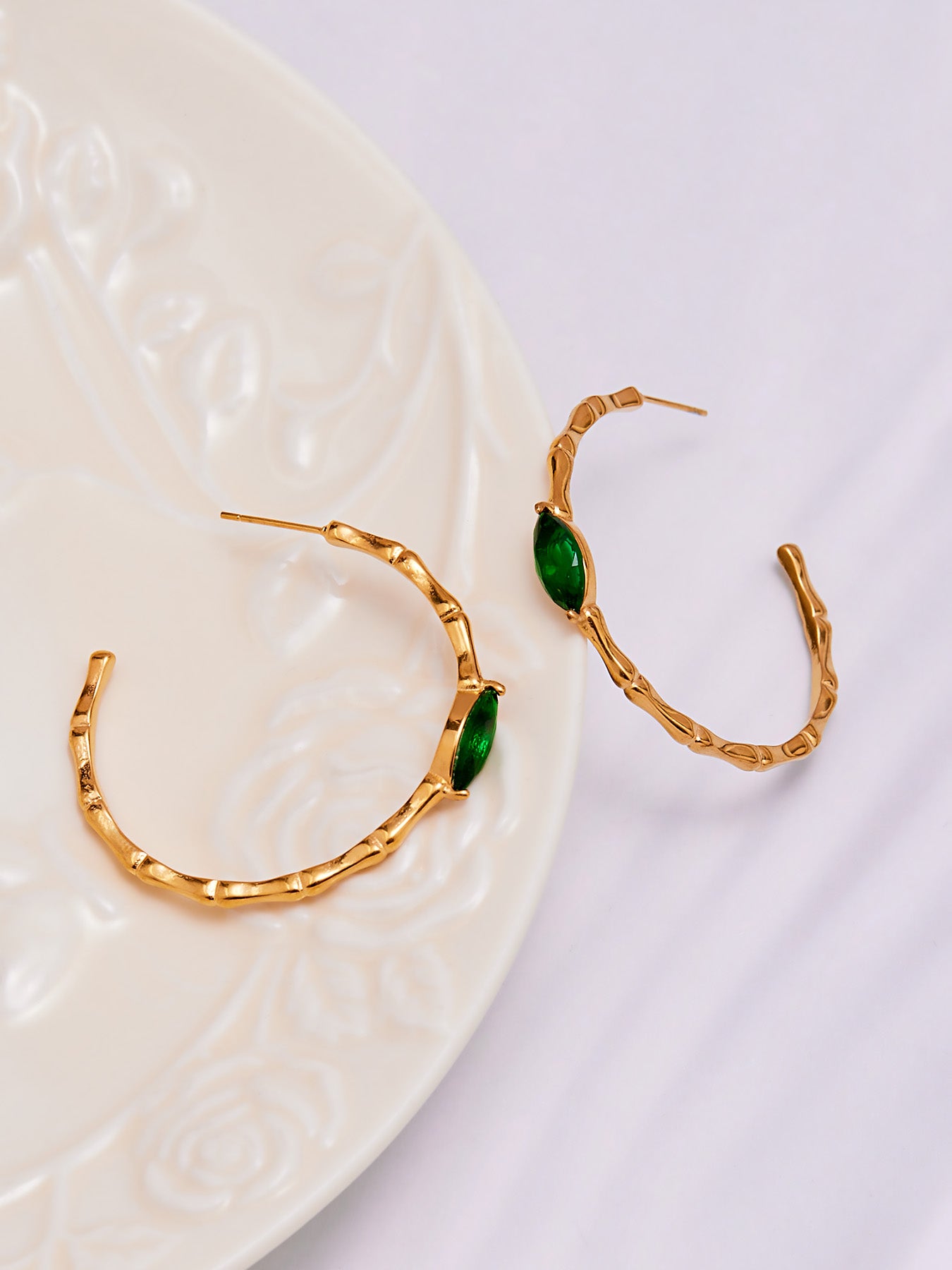 Gold bamboo textured hoop earrings with green stones placed on a soft background
