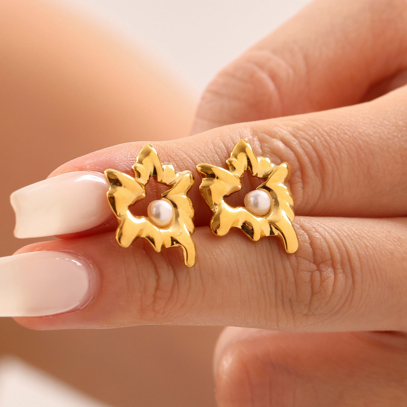 Gold earrings with pearl centers held between fingers against a neutral background