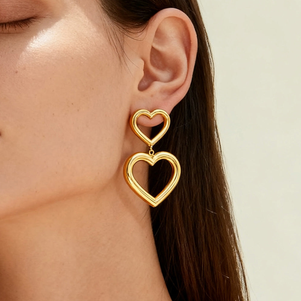 Gold heart-shaped earrings worn by a person with a neutral background