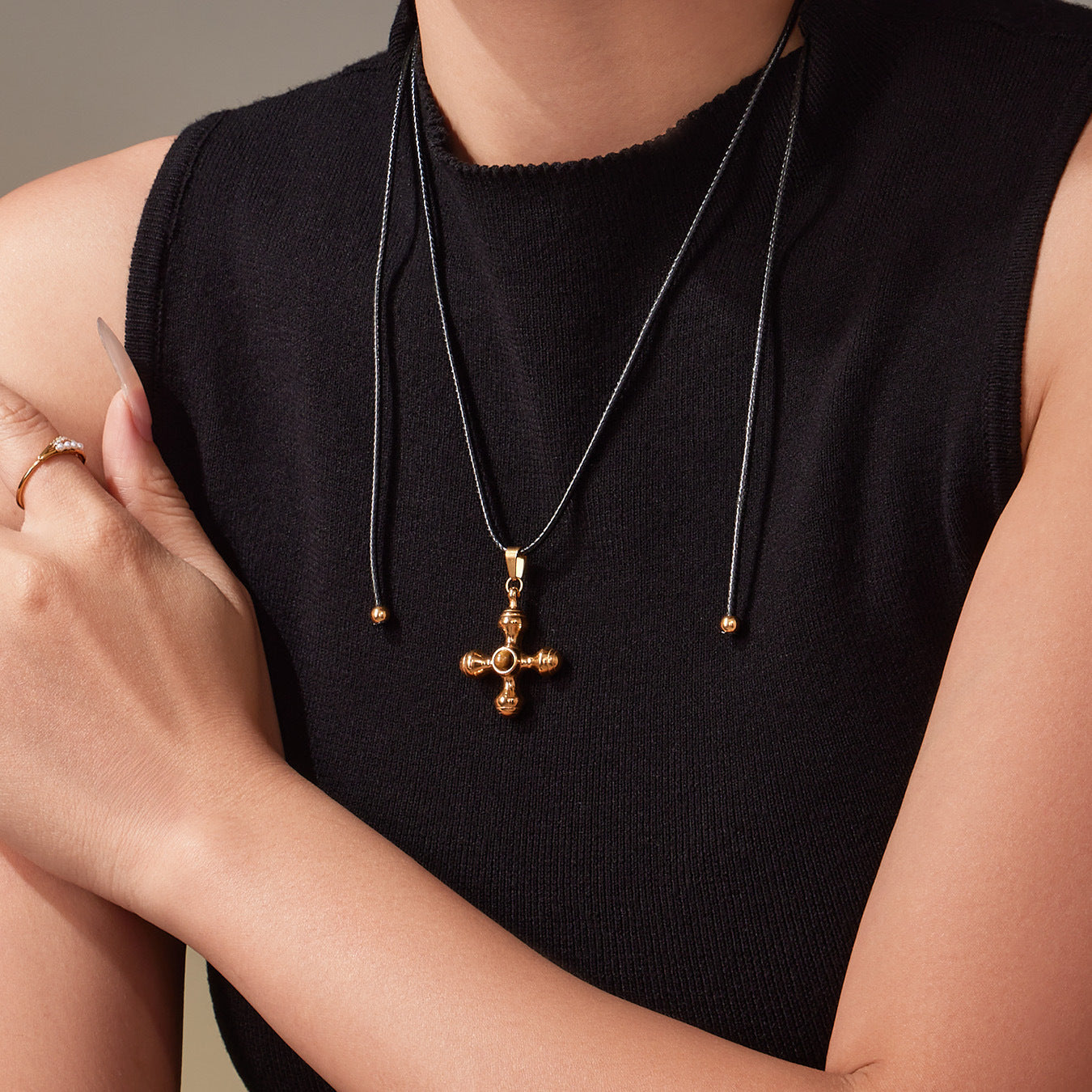 Person wearing a black sleeveless top with a gold cross pendant necklace.