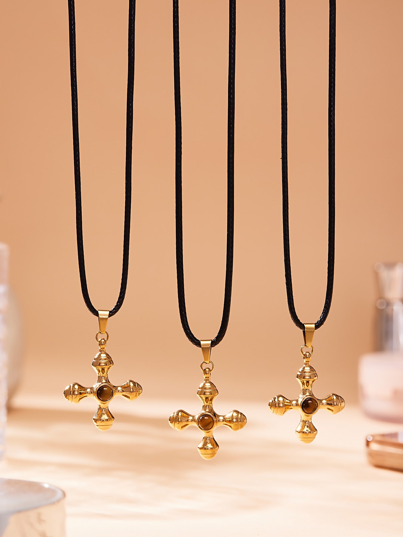 Three gold cross necklaces on black cords against a beige background