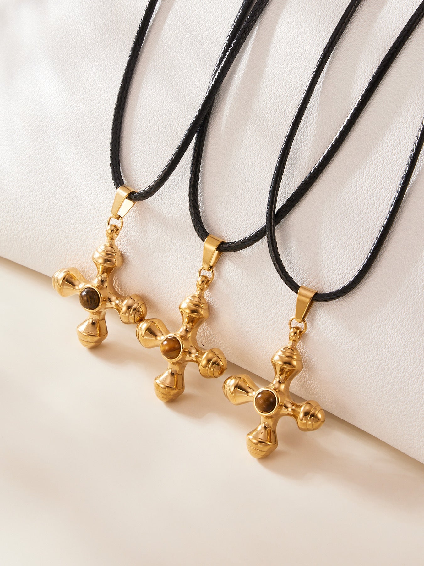 Gold cross-shaped pendants on black cords against a white background