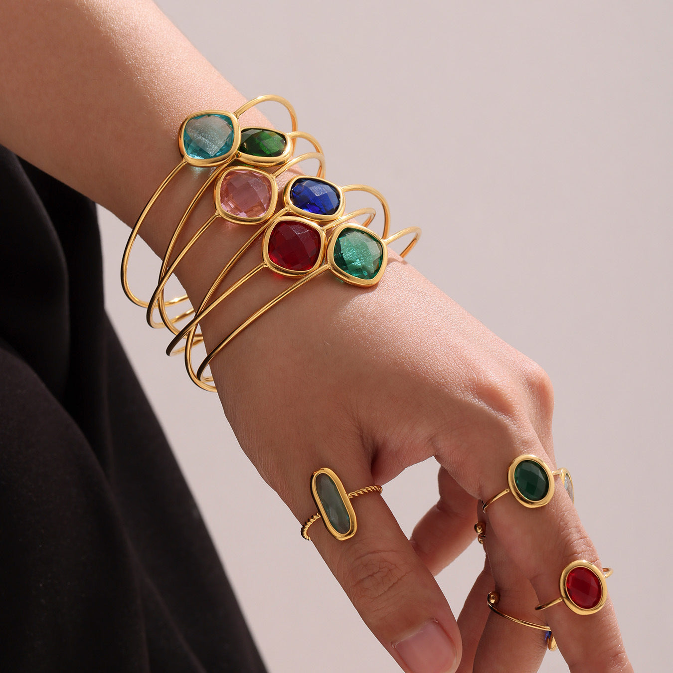 Model wearing multiple gold square Czech glass bracelets in white, green, red, blue, and pink on one arm