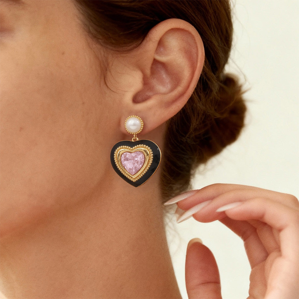Model wearing gold heart stud earrings with pink crystal and pearl top, black enamel heart frame, side profile view