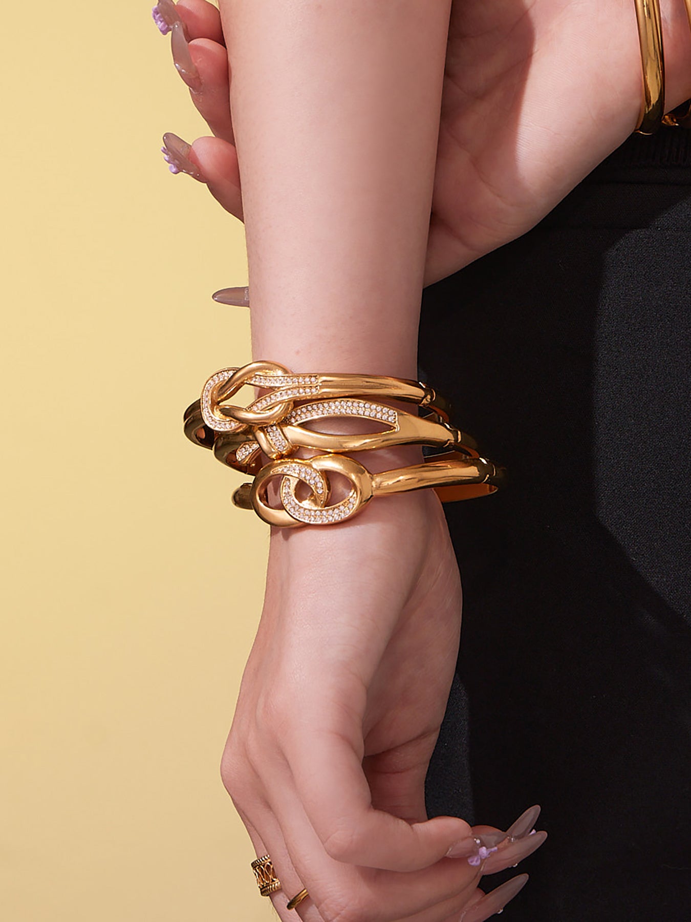 Model styling multiple 18K gold knotted cuff bangles on the wrist, showing how the curved design layers naturally for an elegant, modern everyday look.