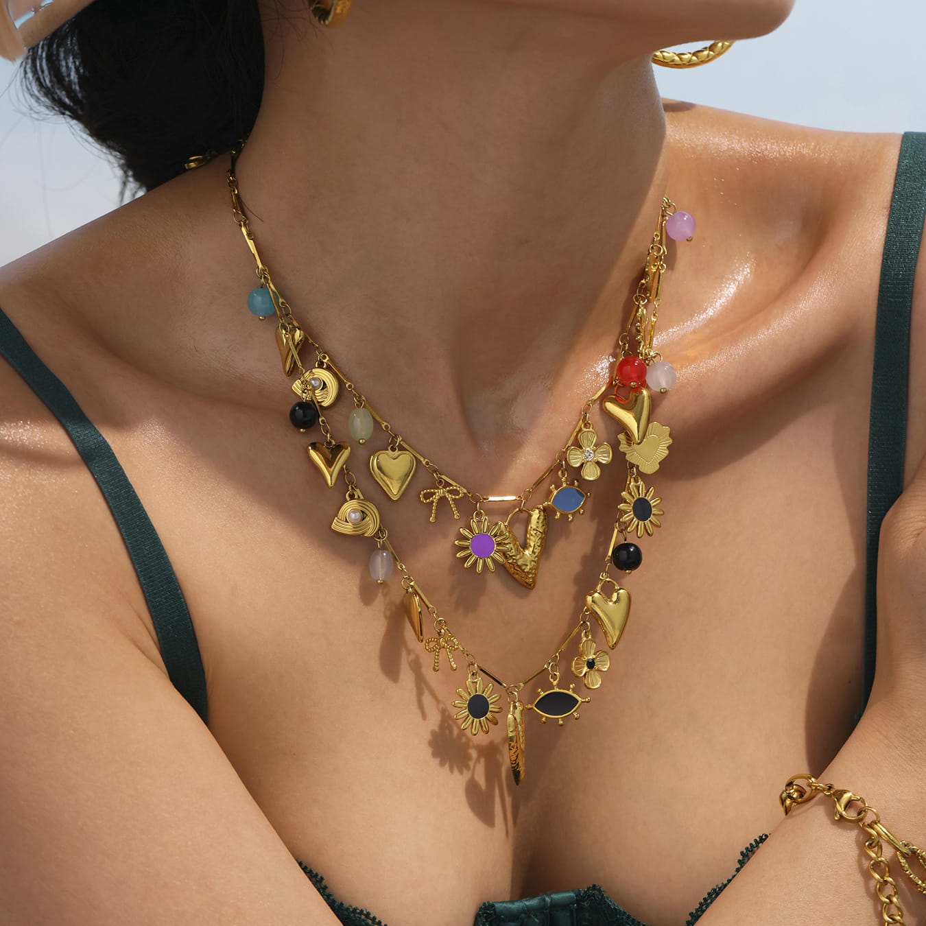 Close-up of model styling waterproof gold sun and moon heart charm necklace with multi-color enamel pendants.