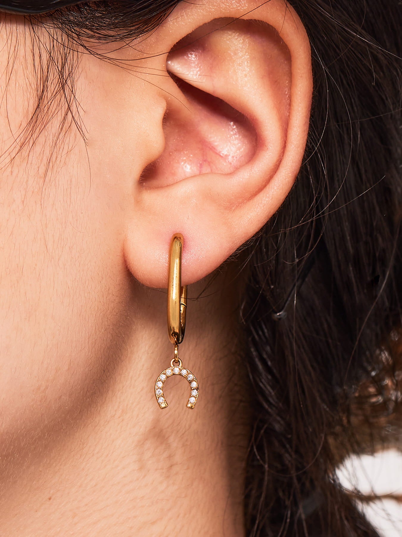 Close-up of an ear wearing a gold hoop earring with a horseshoe charm.