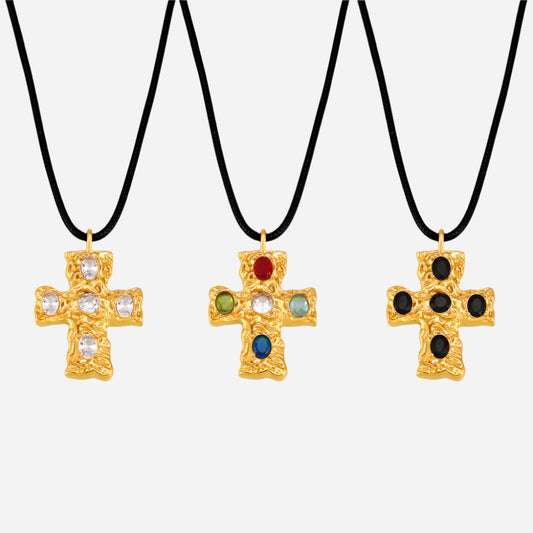 Three gold cross necklaces with colored stones on black cords against a white background