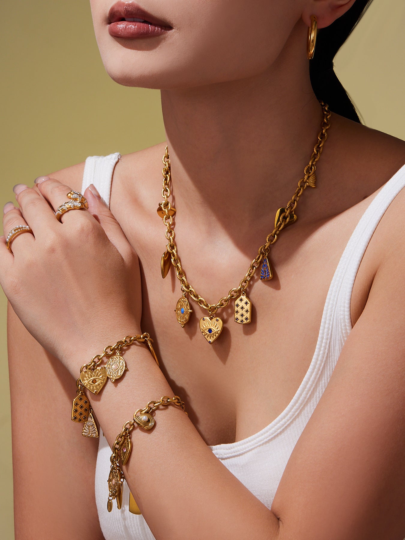Woman wearing gold jewelry including a necklace, bracelet, and rings on a neutral background