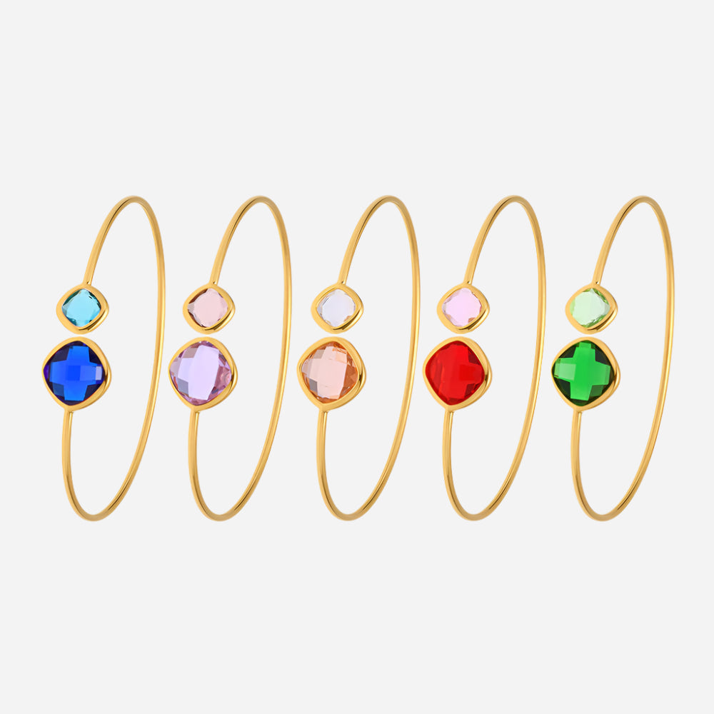 Set of gold bangles with colorful gemstones on a light pink background