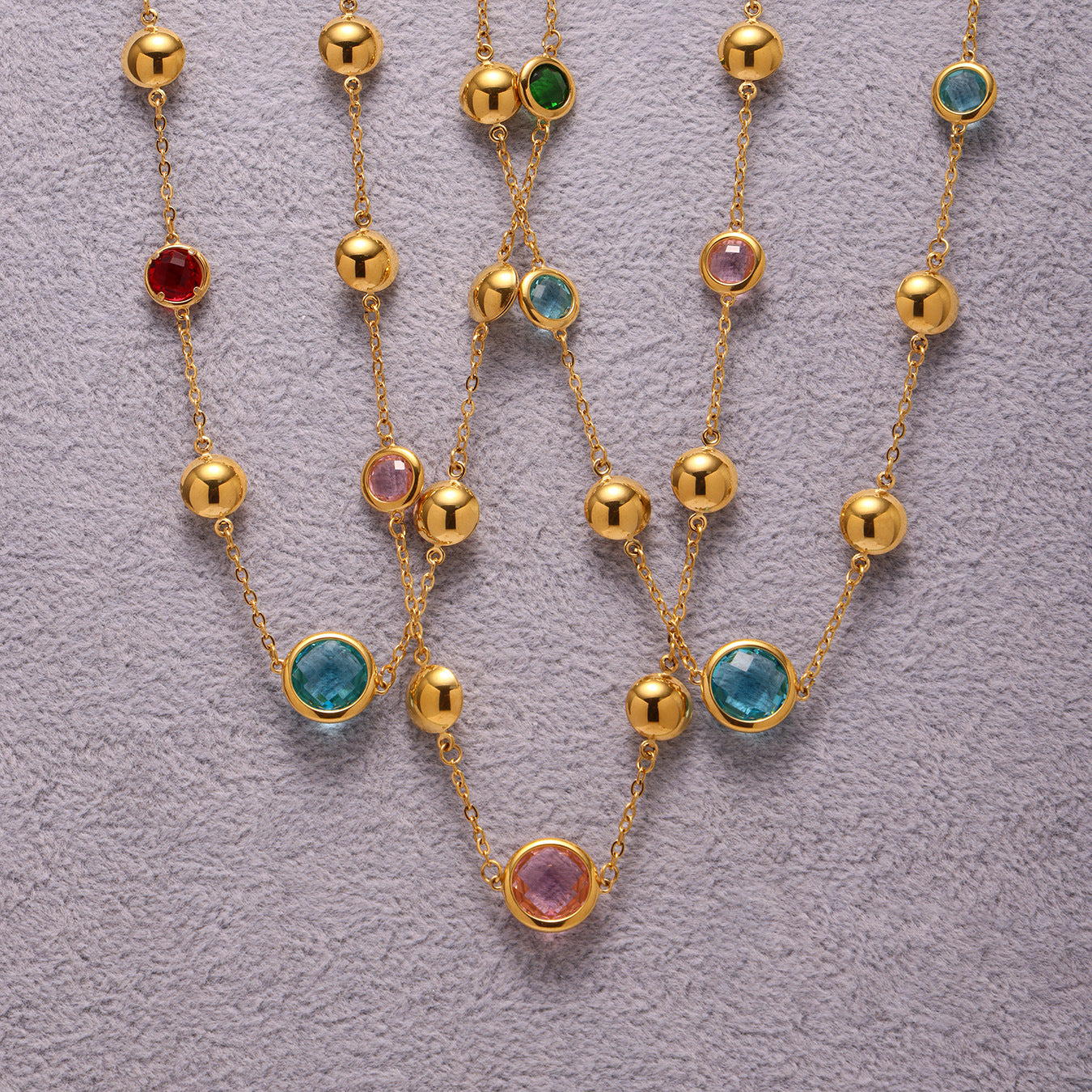 Gold necklaces with colored gemstones on a textured gray background