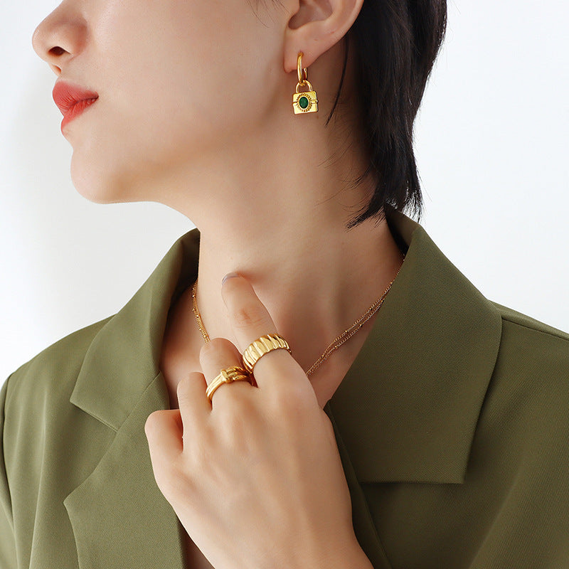 Model wearing the gold padlock hoop earrings with a green gemstone charm, showing how the lock design hangs from the lobe.