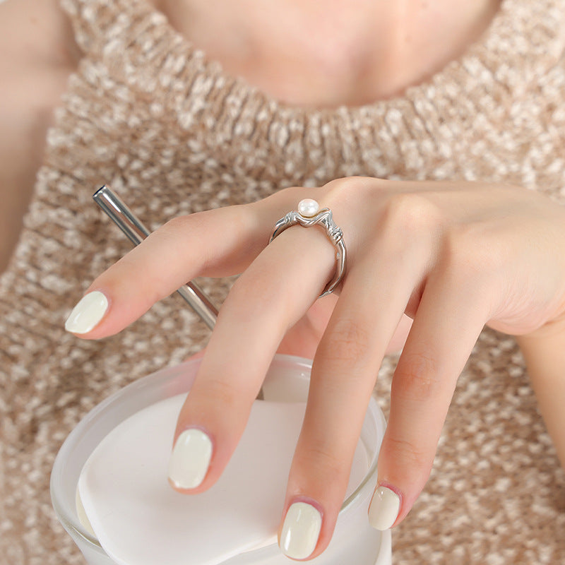 Close-up of a hand wearing a silver ring with a pearl on a neutral background