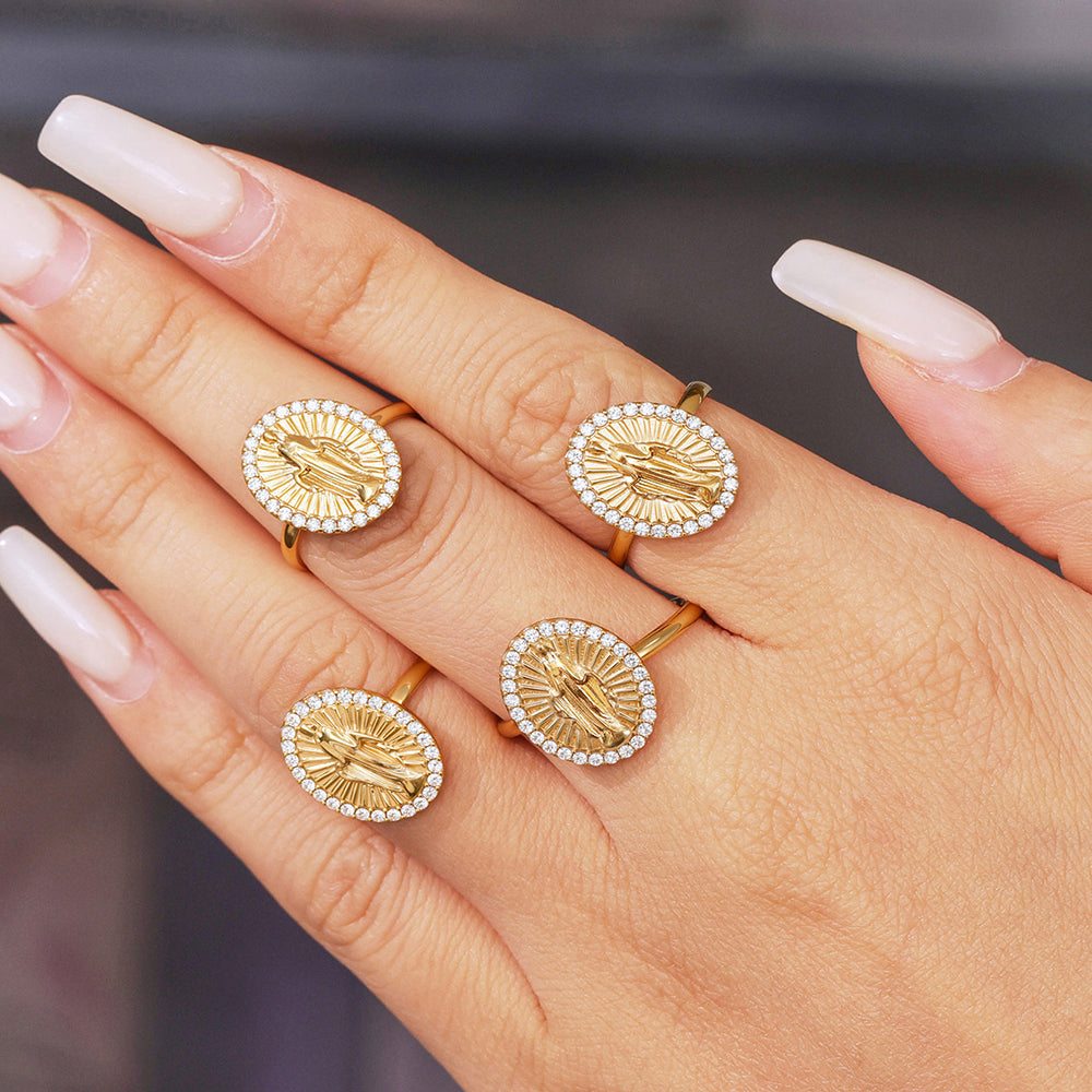 Gold rings with circular designs on a hand against a neutral background