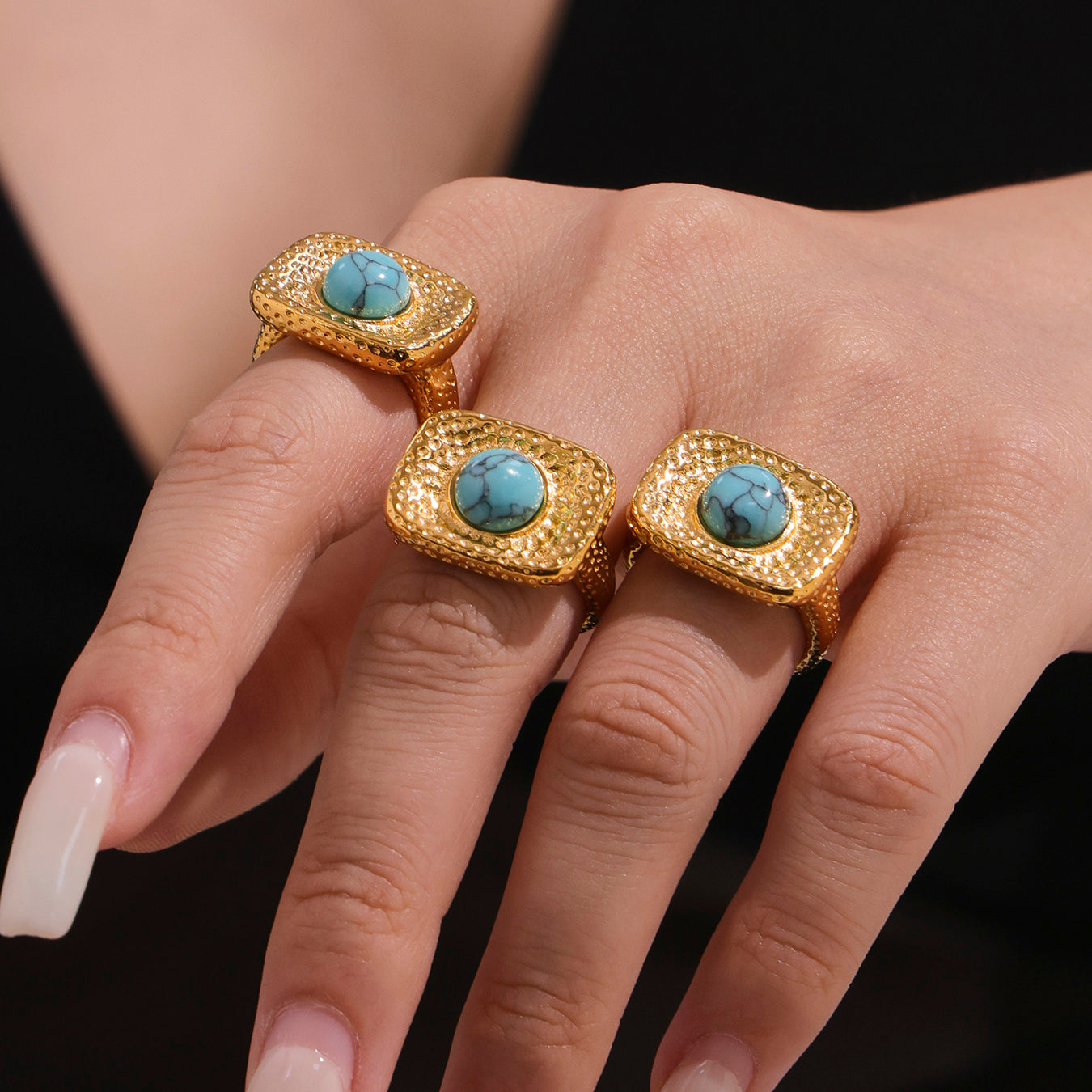 Gold rings with turquoise stones on a hand against a black background