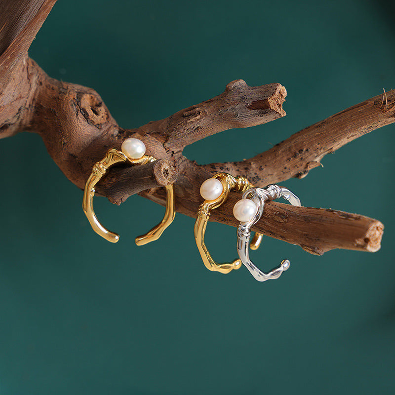 Three pearl earrings in gold and silver on a wooden branch against a teal background