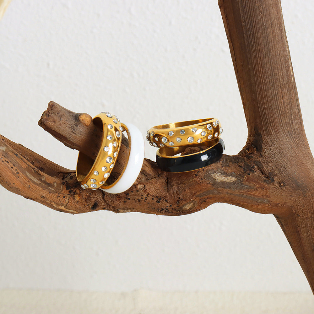 Three rings with gold, black, and white bands on a wooden branch.