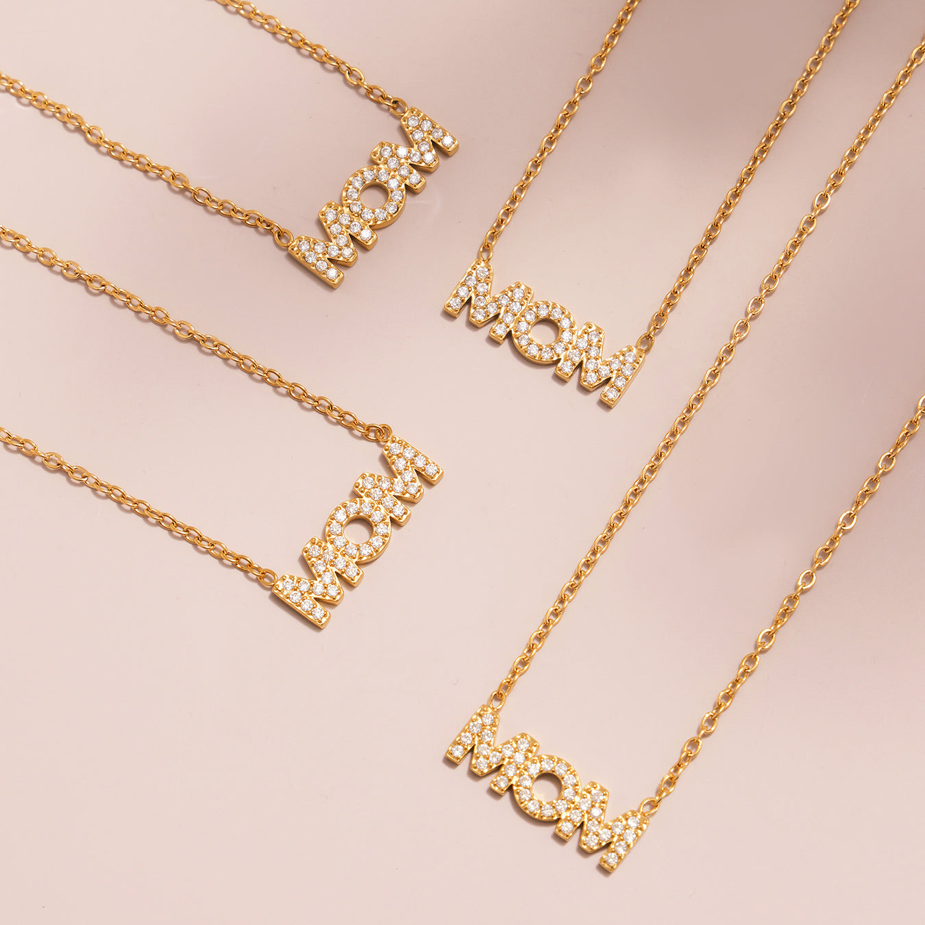 Gold necklaces with 'LOVE' and 'MOM' pendants on a light pink background