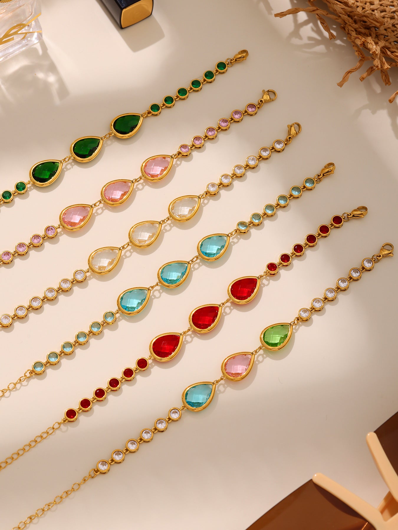 Multiple sea glass teardrop bracelets laid out under sunlight, waterproof gold stainless steel with CZ bezel links