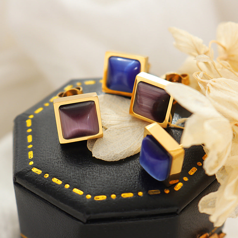 Square cat eye stud earrings in brown and blue displayed on jewelry stand, elegant gold stainless steel minimalist studs
