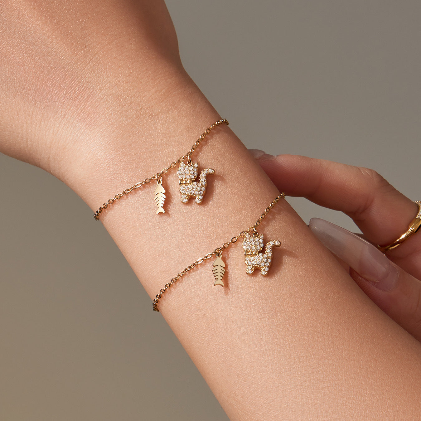 Stacked look with two gold cat bracelets featuring CZ cat and fishbone charms on the wrist.