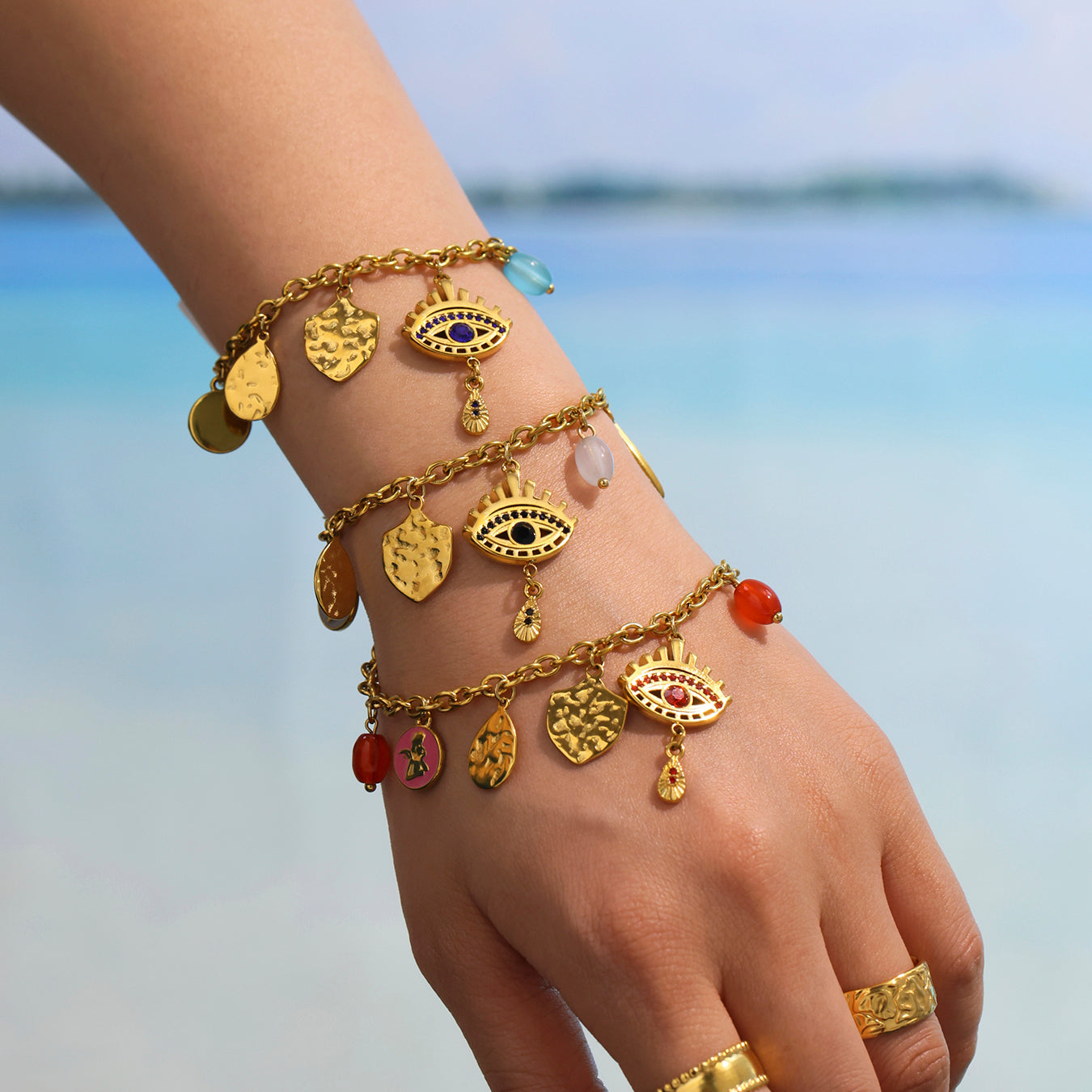 Multiple yellow evil eye bracelets styled on wrist, ocean and waves in the background