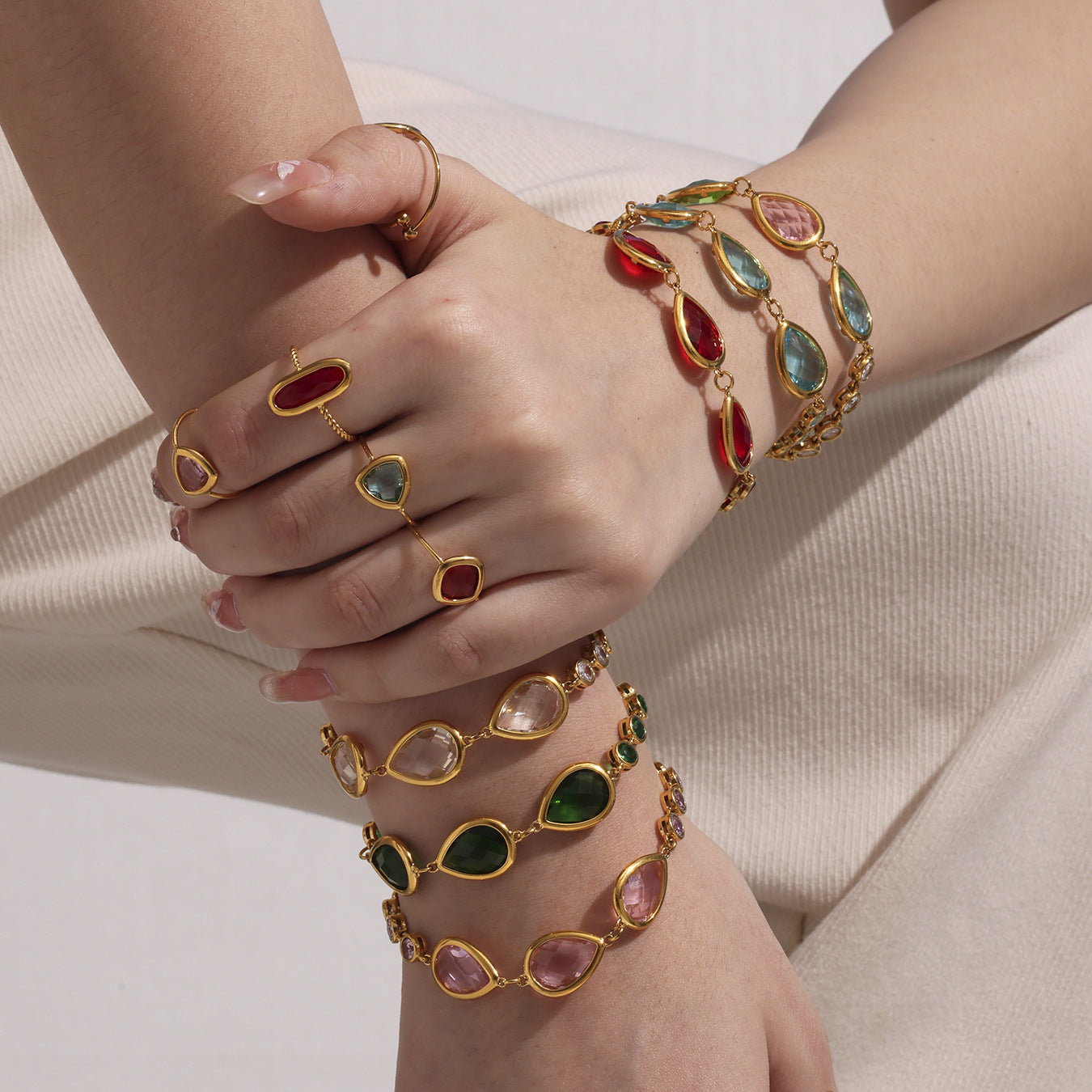 Hand wearing multiple gold bracelets with colorful gemstones on a neutral background