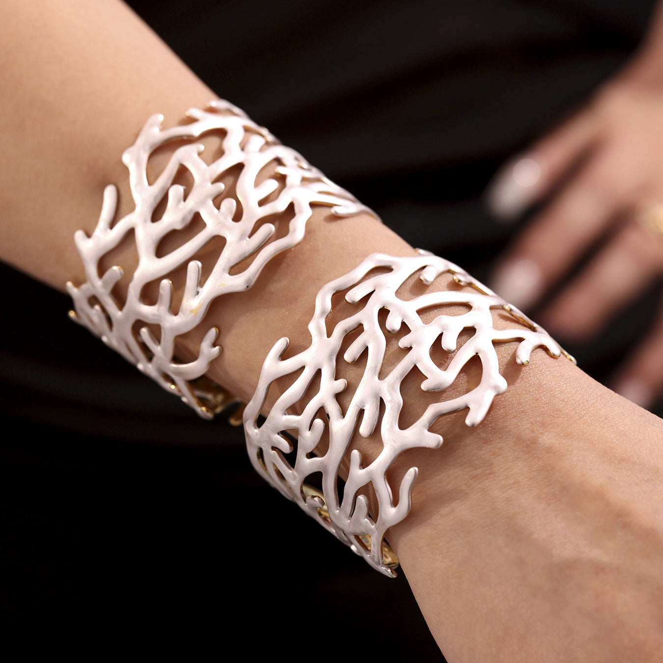 White coral-patterned stainless steel open bangle worn on a wrist against a dark background