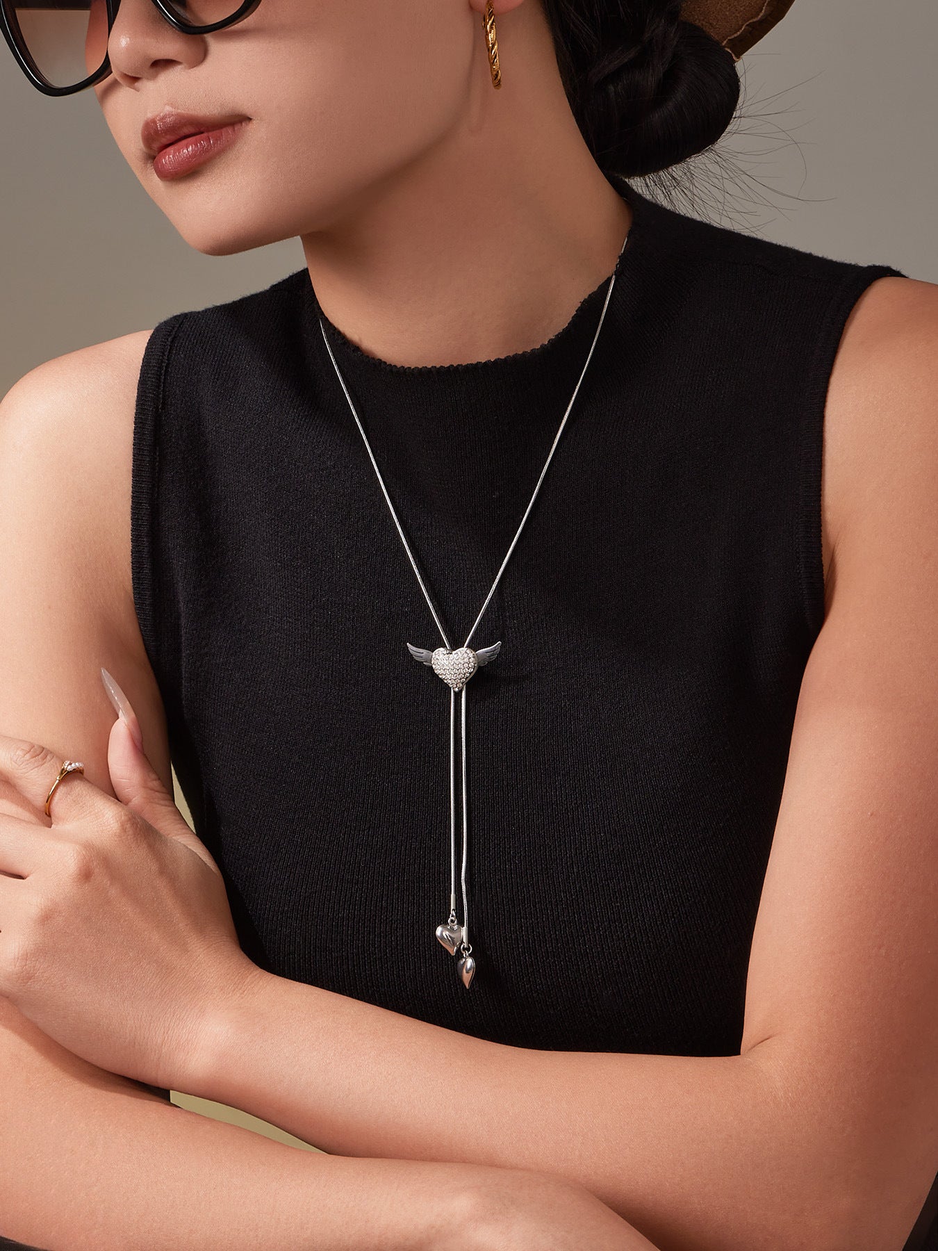 Close-up of the winged puffy heart necklace on the model, highlighting the sparkling CZ angel heart and flowing tassel design.