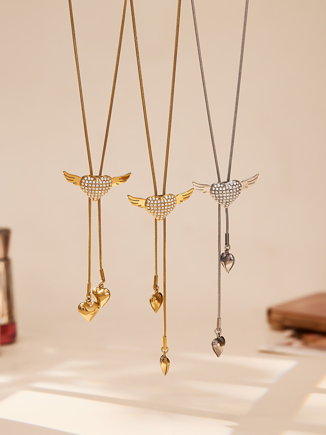 Hanging view of the winged puffy heart necklace showing the adjustable tassel length and movement of the double heart drops.