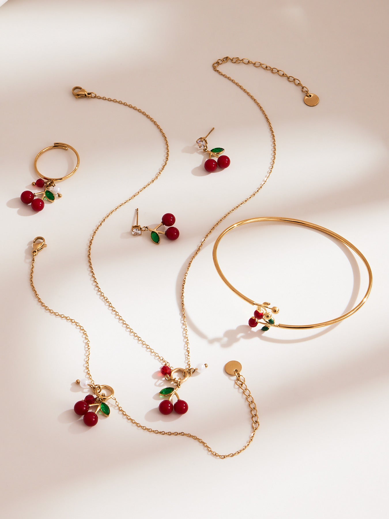 Gold jewelry set with cherry details on a light background