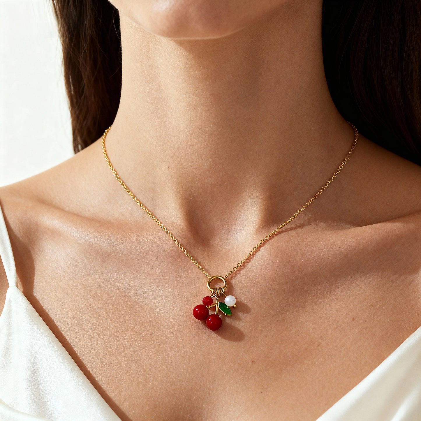 gold cherry necklace on model's neck with red cherry charms, green enamel leaves, and pearl detail, photographed in natural soft light