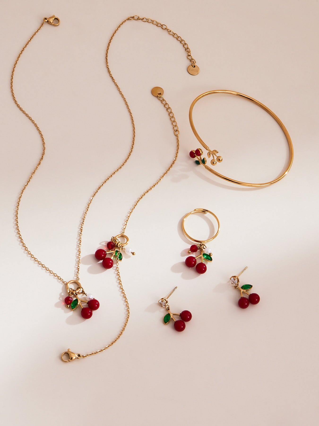 gold cherry necklace, cherry earrings, cherry bracelet, and cherry ring arranged under warm sunlight for product display