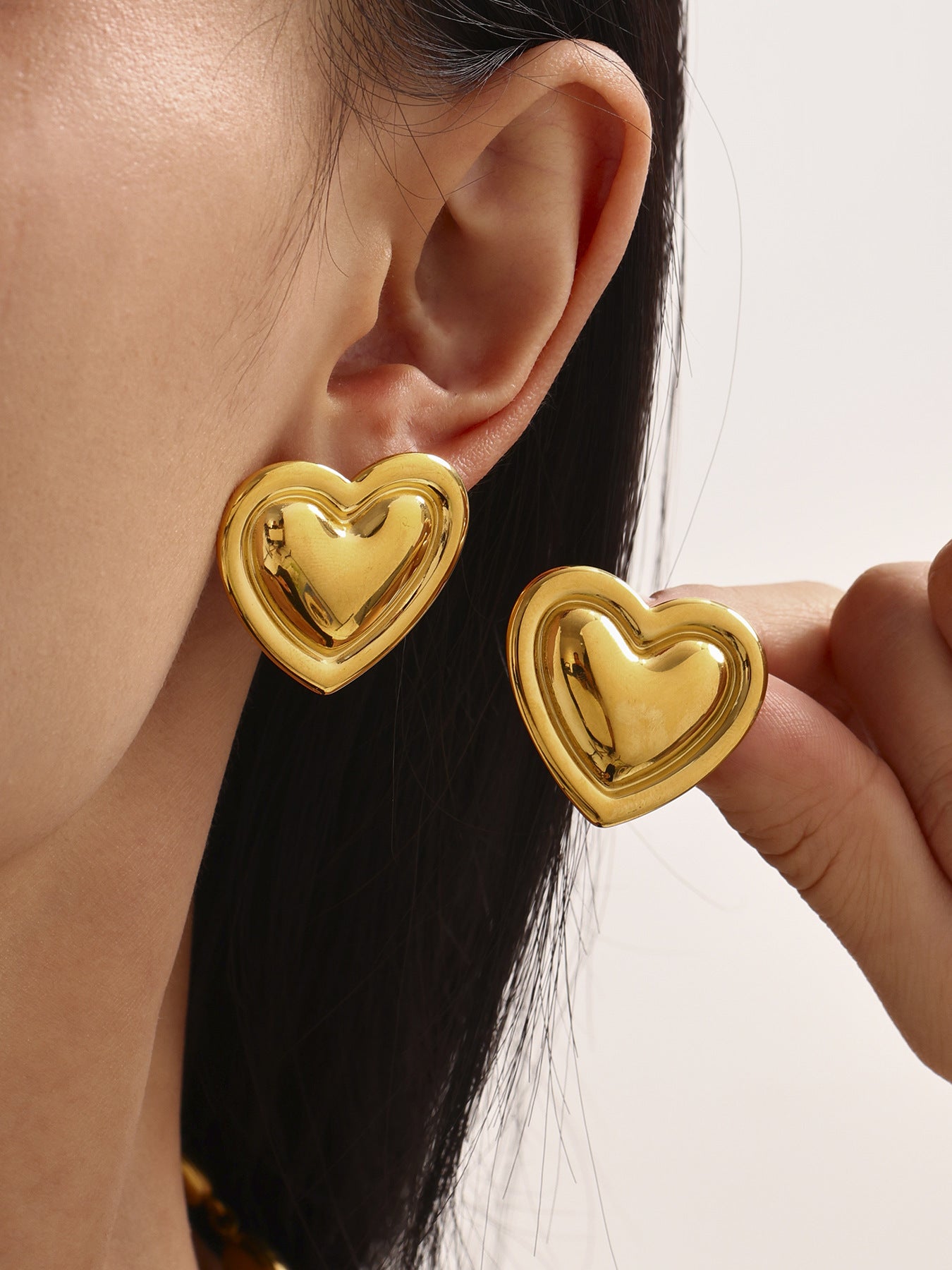 Gold heart-shaped earrings being worn and held by a person.