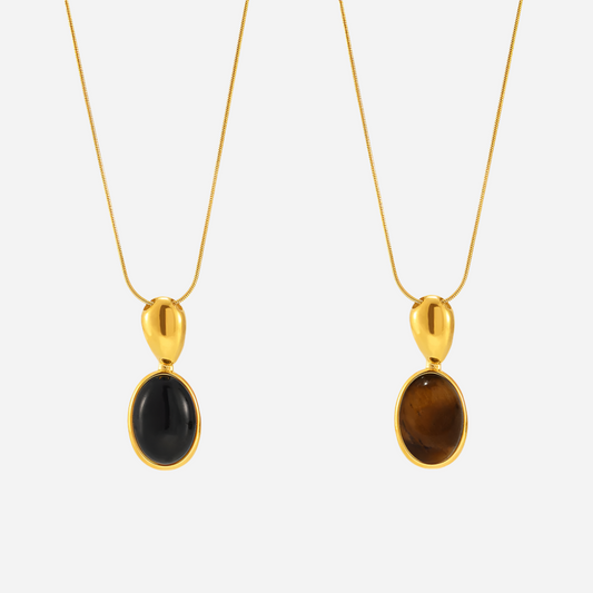 Two gold-plated lariat necklaces with oval pendants, one with a dark tiger eye pendant and the other with a lighter pendant, displayed against a white background.